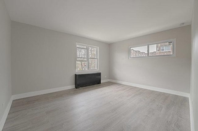 empty room featuring radiator, light wood-style floors, plenty of natural light, and baseboards