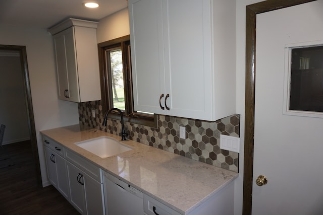 kitchen with white dishwasher, tasteful backsplash, light stone counters, white cabinets, and sink