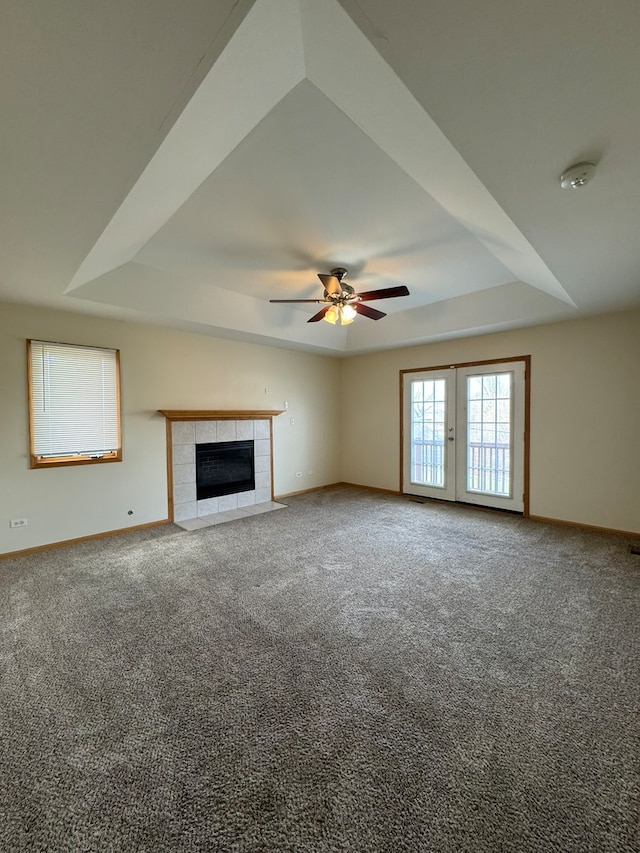 unfurnished living room with carpet floors, a fireplace, french doors, a raised ceiling, and ceiling fan