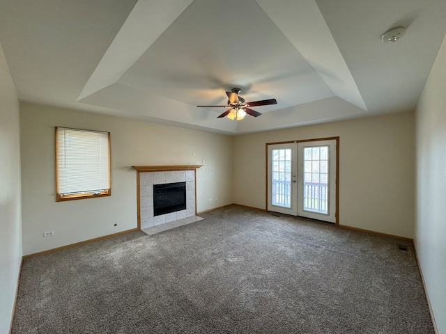 unfurnished living room with ceiling fan, a raised ceiling, carpet floors, and a tiled fireplace