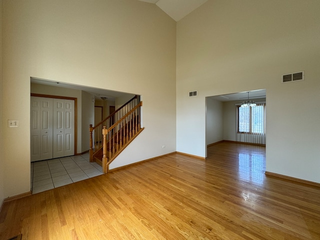 tiled empty room featuring high vaulted ceiling and a notable chandelier