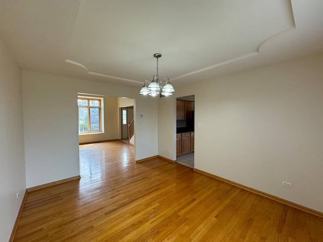 empty room with light hardwood / wood-style floors and a chandelier