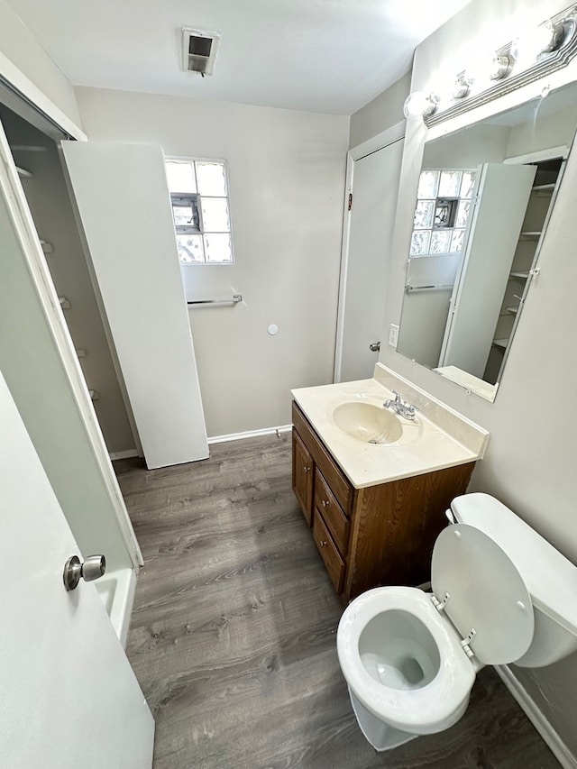 bathroom with wood-type flooring, vanity with extensive cabinet space, and toilet