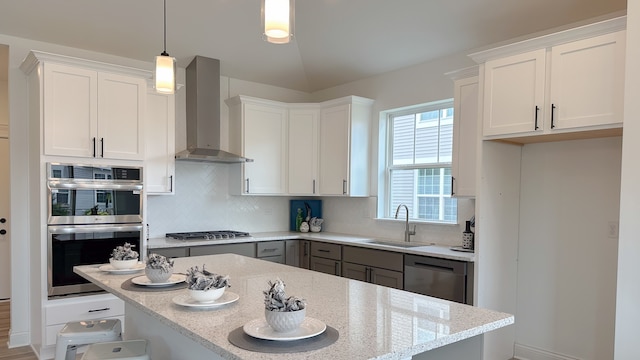 kitchen featuring appliances with stainless steel finishes, hanging light fixtures, wall chimney range hood, white cabinetry, and a sink