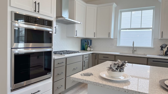 kitchen featuring wall chimney range hood, white cabinetry, stainless steel appliances, and light stone counters