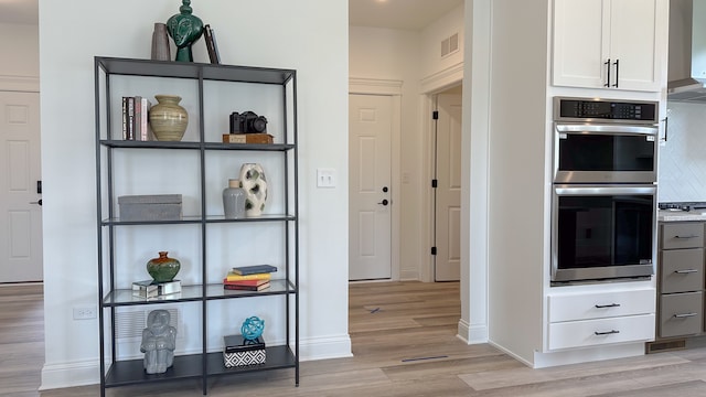 interior space with double oven, visible vents, white cabinetry, light wood-style floors, and light countertops