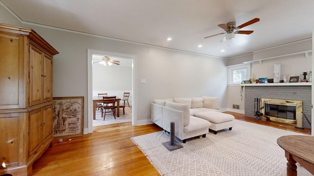 living room with a fireplace, ceiling fan, light wood-type flooring, and ornamental molding