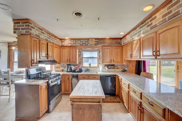 kitchen featuring stainless steel gas stove, sink, brick wall, black dishwasher, and ceiling fan