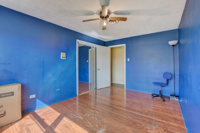 unfurnished bedroom featuring hardwood / wood-style flooring, a closet, a textured ceiling, and ceiling fan