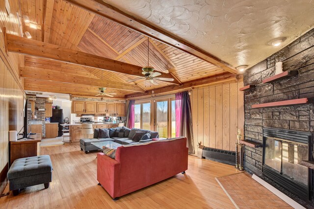 living room with ceiling fan, a stone fireplace, wooden walls, beam ceiling, and light hardwood / wood-style floors