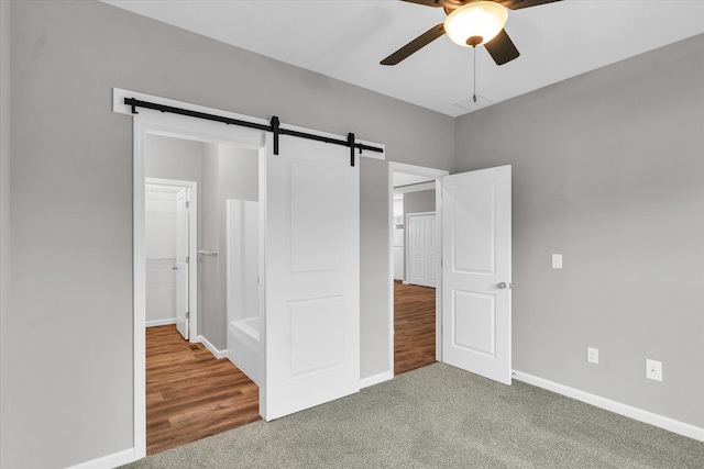 unfurnished bedroom with ceiling fan, a barn door, hardwood / wood-style flooring, a spacious closet, and a closet