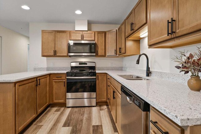 kitchen featuring light stone counters, appliances with stainless steel finishes, sink, light hardwood / wood-style floors, and kitchen peninsula