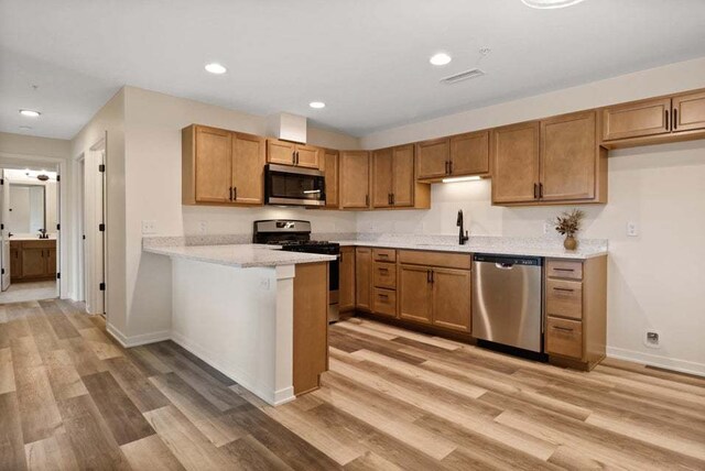 kitchen featuring sink, appliances with stainless steel finishes, light hardwood / wood-style flooring, and light stone countertops