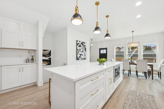 kitchen with pendant lighting, light hardwood / wood-style flooring, white cabinetry, a center island, and stainless steel microwave