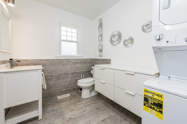 bathroom featuring tile walls, toilet, vanity, hardwood / wood-style floors, and stacked washer and clothes dryer