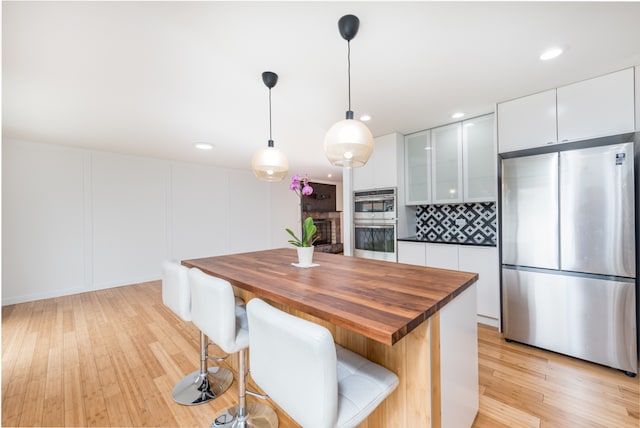 kitchen featuring a fireplace, white cabinetry, a kitchen breakfast bar, stainless steel appliances, and pendant lighting