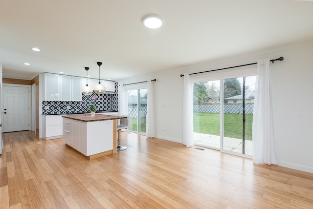 kitchen with light hardwood / wood-style flooring, tasteful backsplash, pendant lighting, and white cabinetry