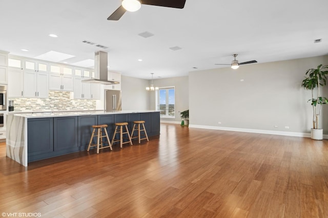 kitchen featuring backsplash, island range hood, white cabinets, decorative light fixtures, and high end refrigerator