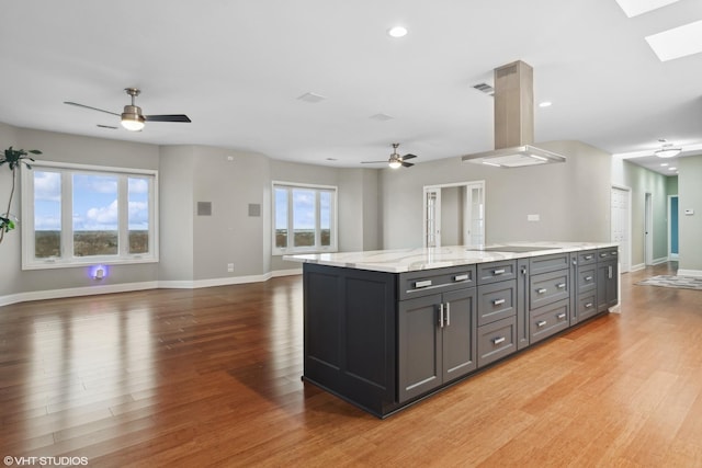 kitchen featuring light stone counters, ceiling fan, a kitchen island, island exhaust hood, and hardwood / wood-style floors