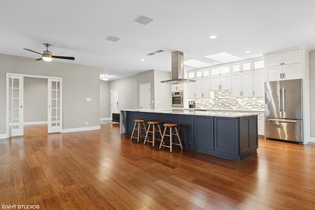 kitchen with island range hood, white cabinets, decorative backsplash, a large island with sink, and stainless steel appliances