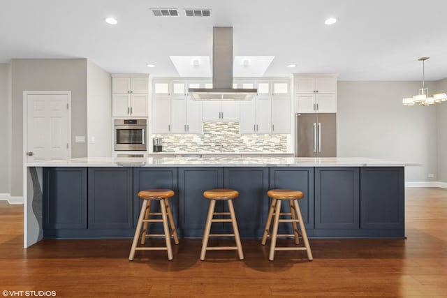 kitchen with appliances with stainless steel finishes, white cabinetry, dark hardwood / wood-style flooring, decorative light fixtures, and a large island with sink