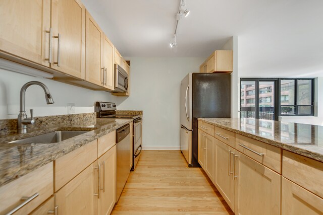 kitchen featuring appliances with stainless steel finishes, light hardwood / wood-style flooring, track lighting, light stone counters, and light brown cabinetry