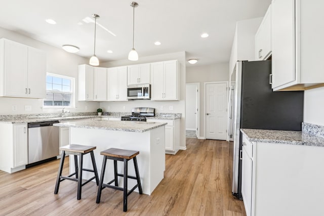 kitchen with stainless steel appliances, a kitchen breakfast bar, white cabinetry, and light hardwood / wood-style floors