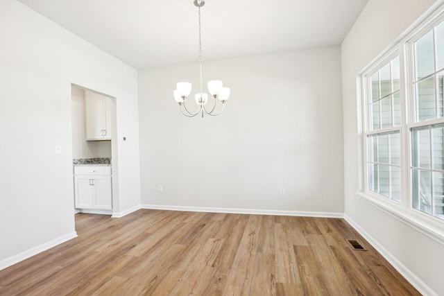 unfurnished dining area with a notable chandelier and light hardwood / wood-style flooring