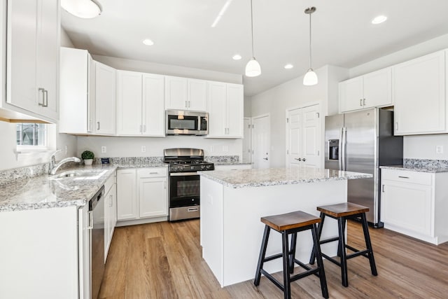 kitchen featuring a kitchen island, stainless steel appliances, sink, white cabinetry, and light wood-type flooring