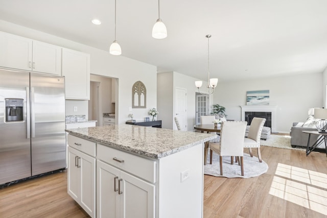 kitchen with white cabinets, light hardwood / wood-style flooring, light stone counters, built in fridge, and pendant lighting