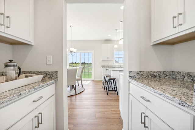 kitchen with light wood-type flooring, white cabinetry, a chandelier, light stone counters, and hanging light fixtures