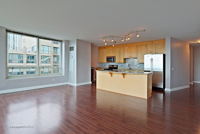 kitchen featuring stainless steel appliances, track lighting, tasteful backsplash, dark hardwood / wood-style flooring, and a breakfast bar