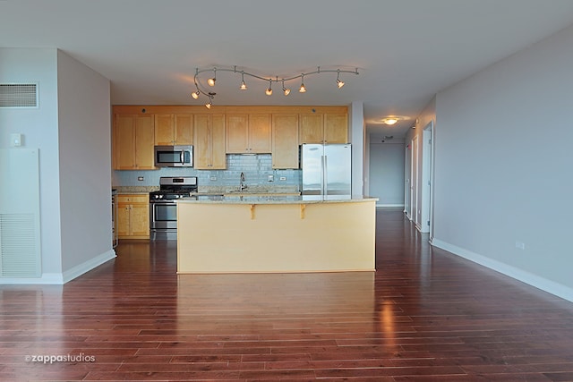 kitchen with light brown cabinets, appliances with stainless steel finishes, tasteful backsplash, dark wood-type flooring, and rail lighting