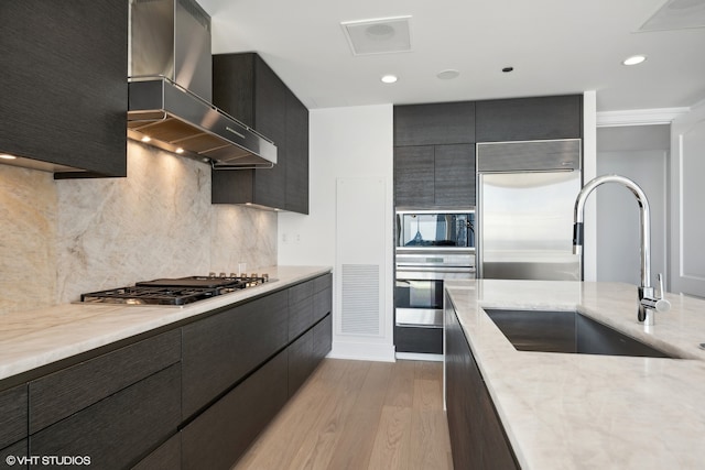 kitchen with light hardwood / wood-style floors, tasteful backsplash, built in appliances, wall chimney range hood, and sink