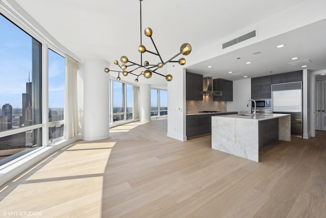 kitchen featuring hanging light fixtures, wall chimney exhaust hood, light hardwood / wood-style floors, and backsplash