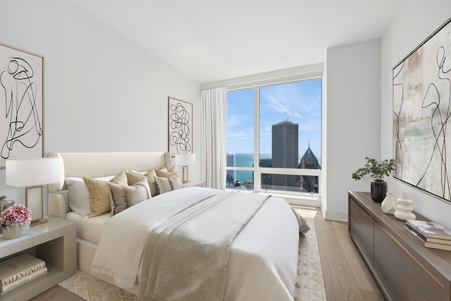 bedroom with a water view, expansive windows, and light hardwood / wood-style flooring