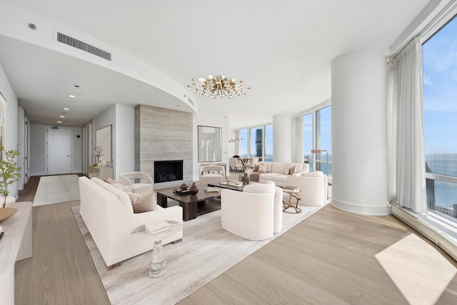 living room featuring a notable chandelier, light hardwood / wood-style floors, a large fireplace, and a wealth of natural light