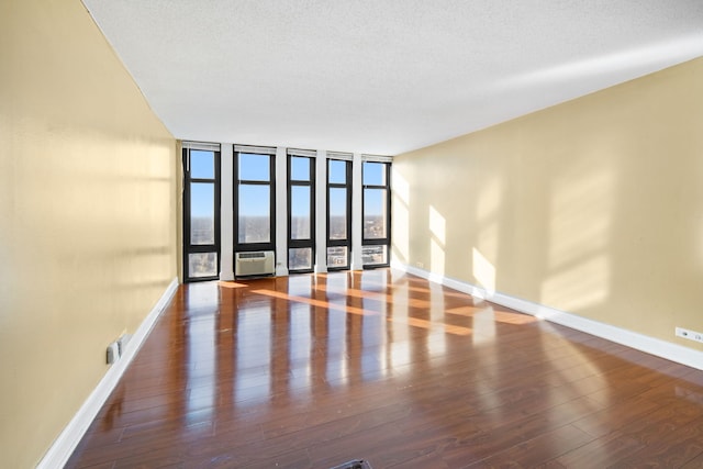 spare room with floor to ceiling windows, dark hardwood / wood-style floors, a wall mounted air conditioner, and a textured ceiling