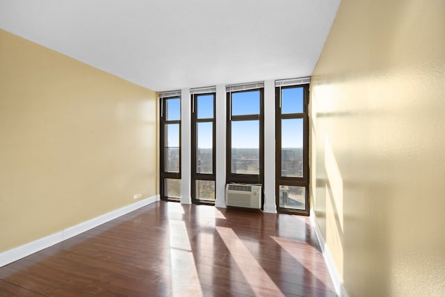 empty room featuring expansive windows, a wall mounted air conditioner, a wealth of natural light, and dark hardwood / wood-style floors