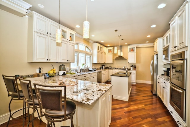 kitchen with a kitchen bar, a kitchen island with sink, appliances with stainless steel finishes, decorative light fixtures, and dark hardwood / wood-style flooring