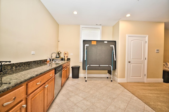 kitchen with dark stone countertops, light carpet, sink, and stainless steel dishwasher