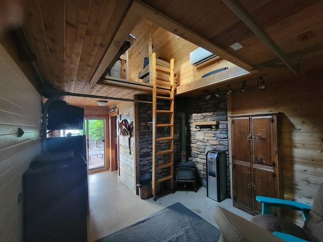 interior space with wooden walls, wood ceiling, concrete floors, and a wood stove