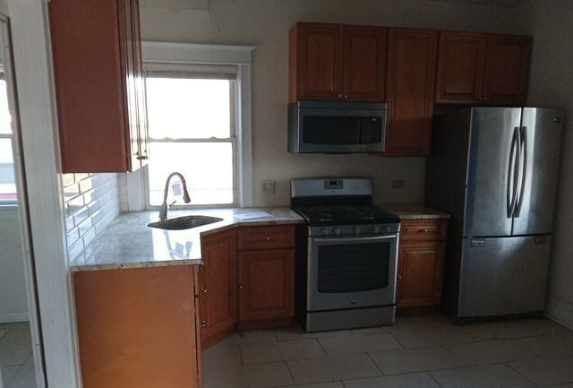 kitchen with appliances with stainless steel finishes, sink, light stone countertops, and light tile floors