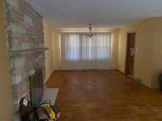 unfurnished living room featuring a stone fireplace, a notable chandelier, and hardwood / wood-style floors