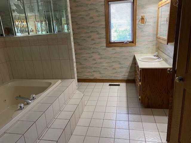 bathroom featuring tile patterned flooring, vanity, and a relaxing tiled tub