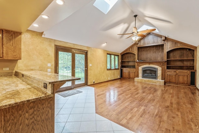 unfurnished living room with built in shelves, vaulted ceiling with skylight, light tile patterned floors, ceiling fan, and a fireplace