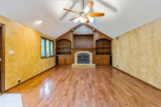 unfurnished living room with built in features, ceiling fan, hardwood / wood-style floors, a large fireplace, and vaulted ceiling