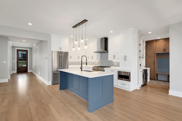 kitchen with appliances with stainless steel finishes, a center island with sink, light hardwood / wood-style floors, and wall chimney range hood