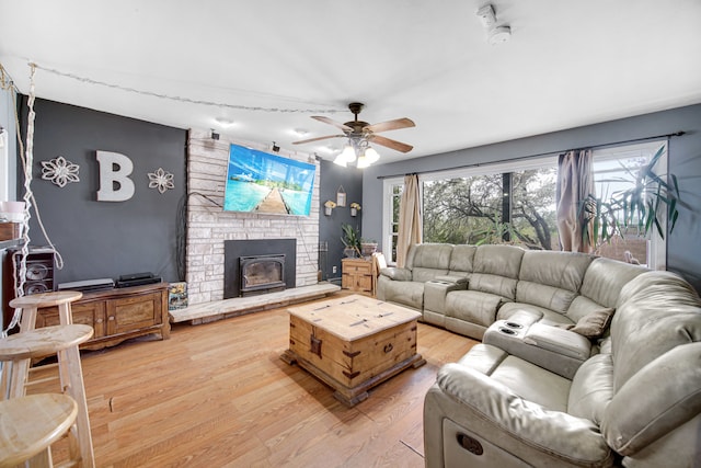 living room featuring a stone fireplace, ceiling fan, and hardwood / wood-style floors