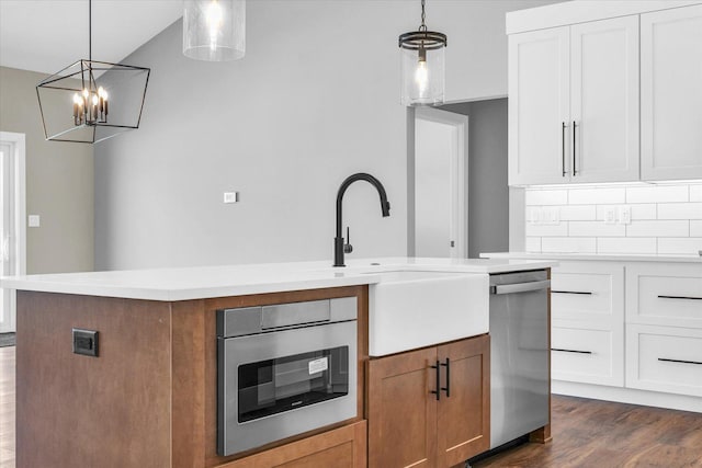 kitchen with stainless steel appliances, decorative light fixtures, white cabinets, decorative backsplash, and a center island with sink